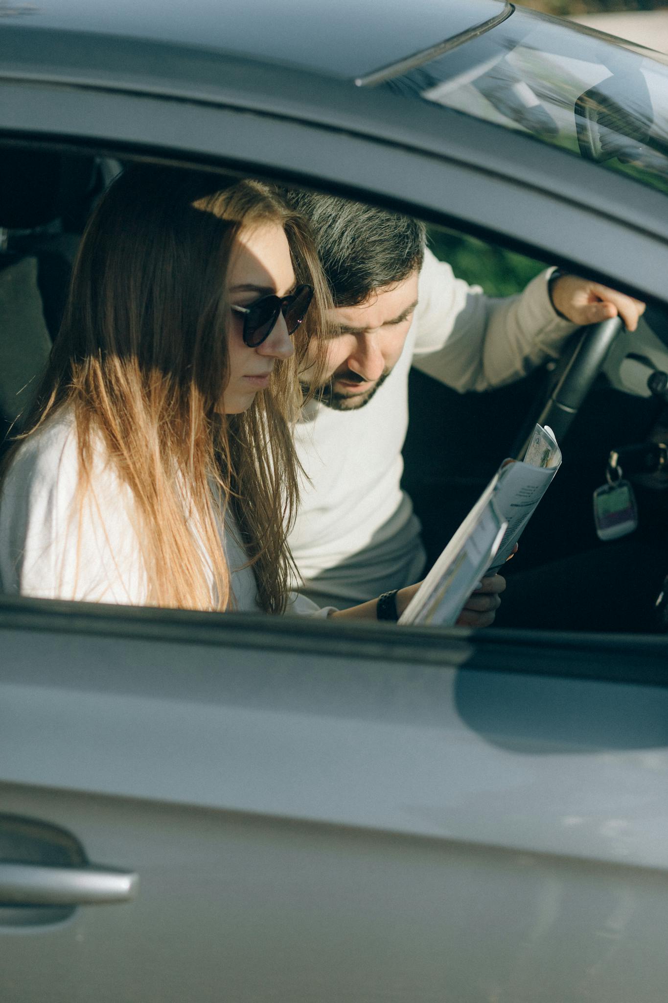 A young couple reading a map inside a car, planning their travel route.