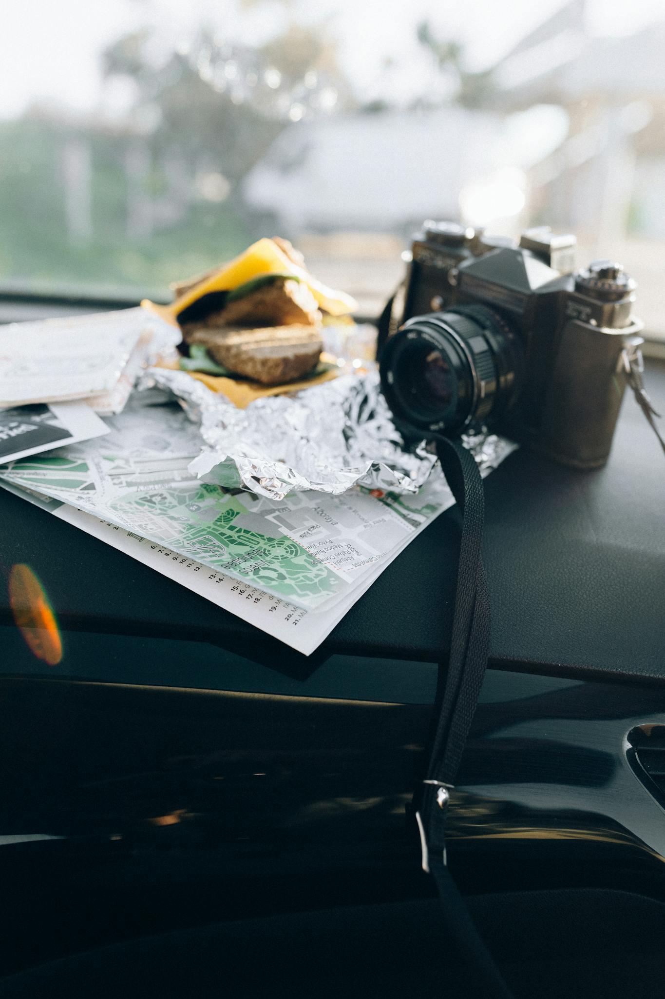 Vintage camera with maps and burger on car dashboard, perfect for a road trip adventure.